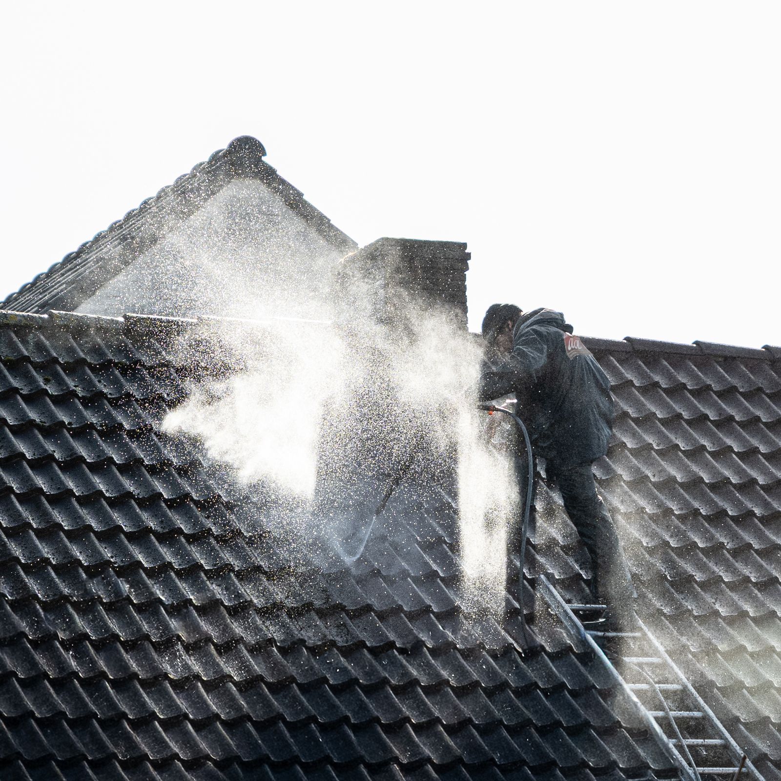 Pressure washing a roof surface in progress